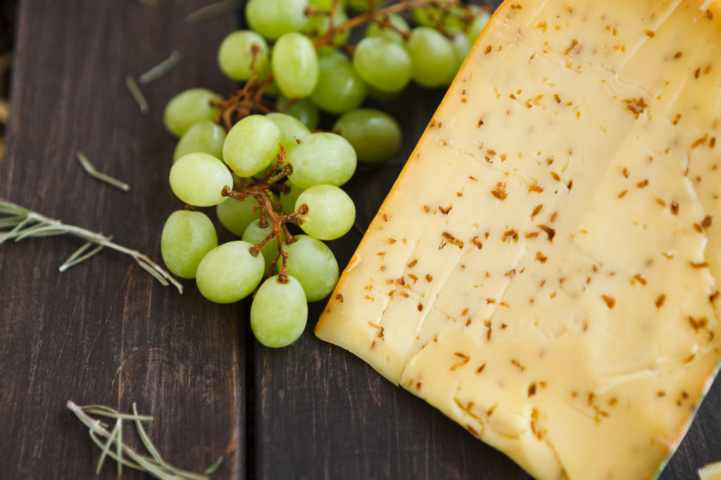Gouda pesto cheese closeup. Still life with white grapes and rosemary on rustic wood background, copy space.