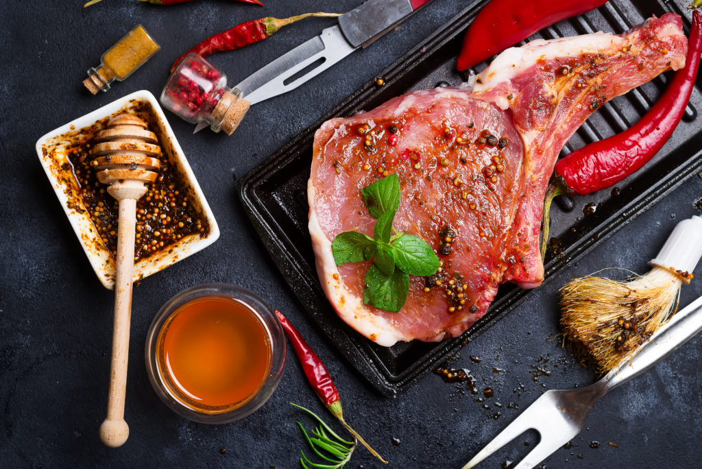 Selection of marinated meat for grilling in a grill display serving a slice with vegetables and honey on a concrete dark background. Top view with copy space