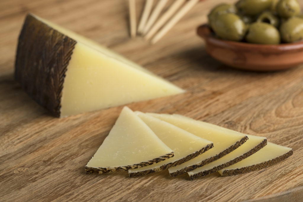 Slices of traditional Spanish Manchego cheese and olives on the background